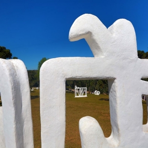 Detalhe da escultura "Horizonte" de Felícia Leirner onde, por meio da estrutura vasada, é possível ver o jardim de esculturas.