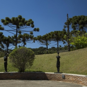 Semicírculo com esculturas feitas em bronze. Ao fundo há um jardim e árvores nativas.