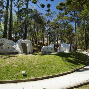Jardim com esculturas da coleção "habitáculos" de Felícia Leirner, as quais estão dispostas em meio a natureza com árvores e vegetação nativa.