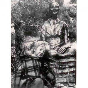 A imagem está em preto e branco e mostra Felícia Leirner, em sua meia idade, sentada no chão e com a cabeça encostada sobre os joelhos de uma de suas esculturas.