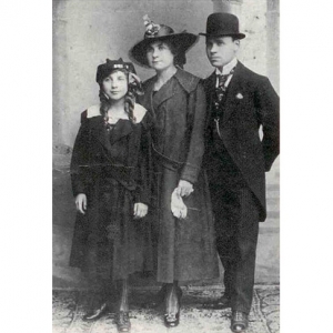 A imagem está em preto e branco e mostra Felícia Leirner criança ao lado de seus pais. Ela é uma menina que veste um sobretudo preto. Sua mãe, pouco mais alta que ela, também veste um sobretudo e um chapéu. Ao lado há um homem de terno, gravata e chapéu.