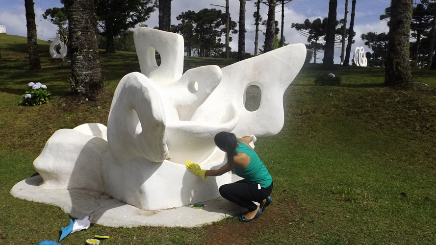 Um mulher está fazendo a manutenção e limpeza da escultura " O Pássaro" de Felícia Leirner.