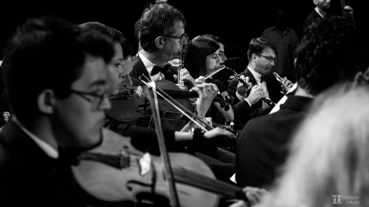 A foto está em preto e branco e mostra músicos tocando instrumentos de sobro e corda.