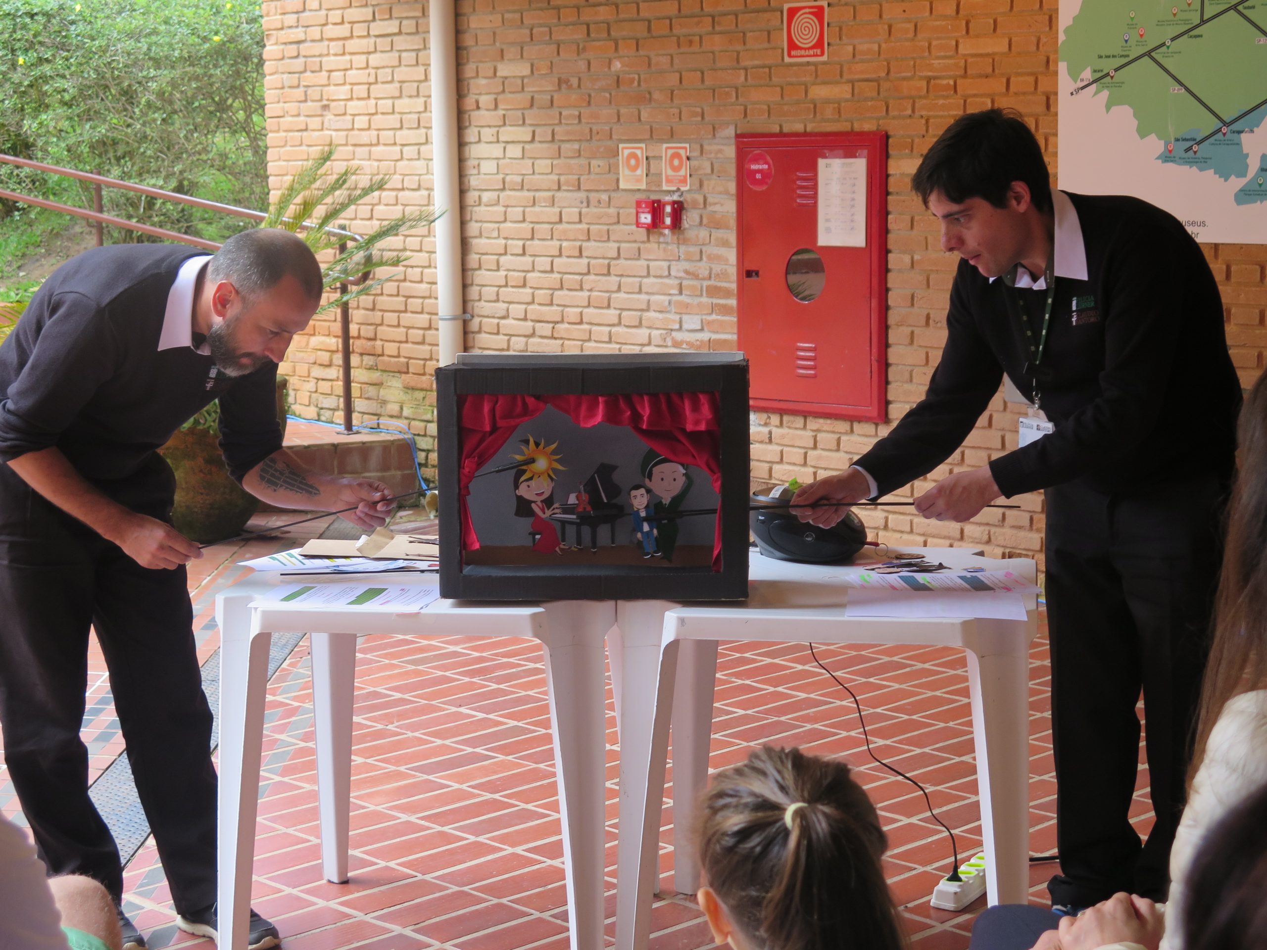 Dois educadores estão apresentando o teatro de papel da história de Claudio Santoro.