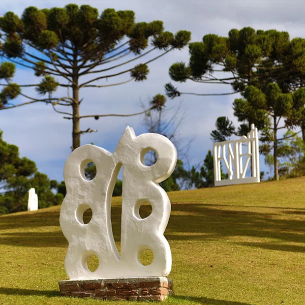 Escultura "Composição" de Felícia Leirner feira em cimento branco armado. A escultura está presente em um jardim com árvores e vegetação nativa.