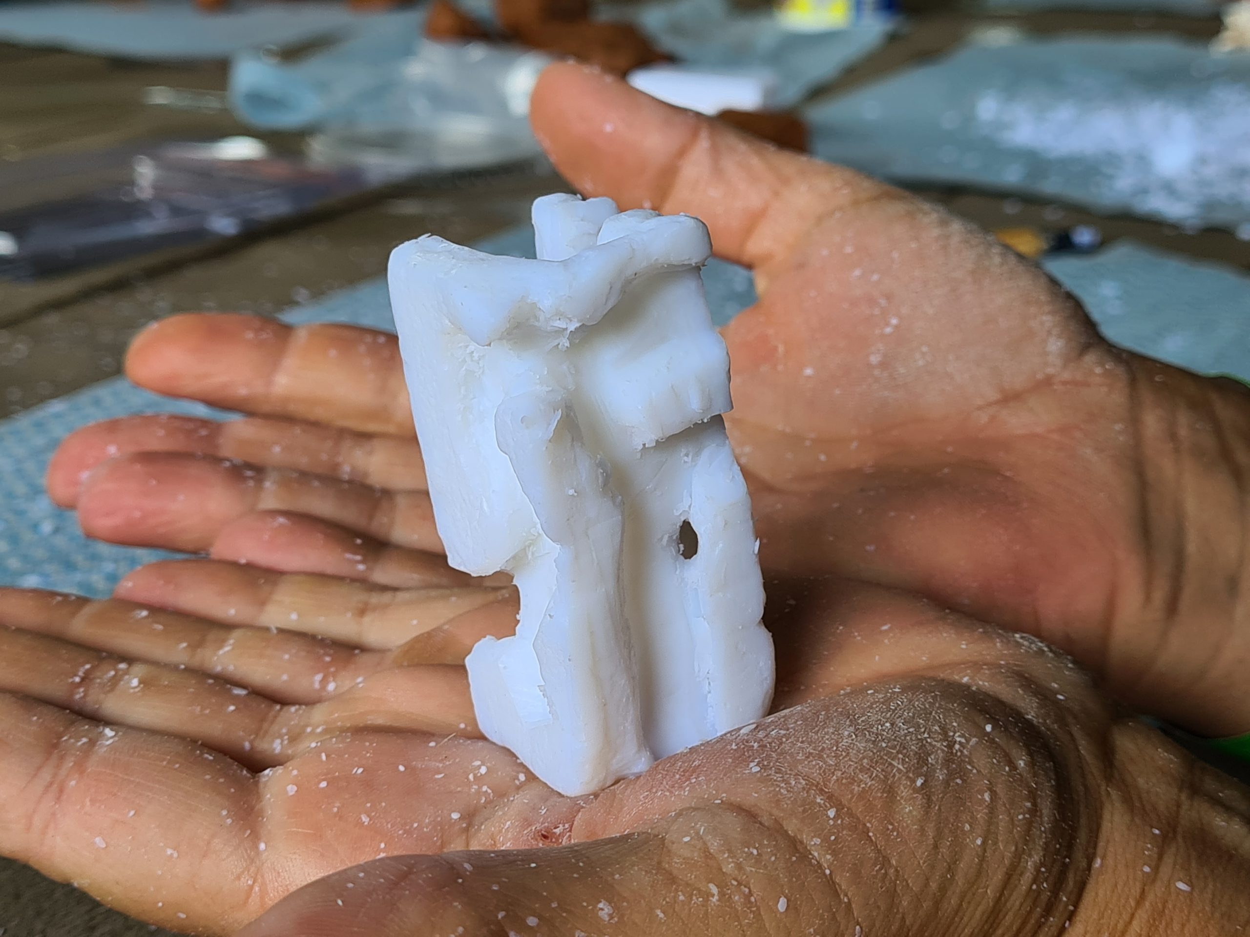 A imagem de duas mãos segurando uma mini escultura em forma geométricas feita de sabão de pedra.