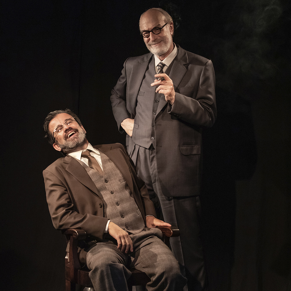 A foto mostra Claudio Fontana, à esquerda, sentado em uma cadeira marrom. Ele veste terno marrom e usa óculos. Odilon Wagner está em pé, à direita, veste terno completo cinza e está usando óculos e segura um charuto na mão direita. Ambos estão sorrindo.