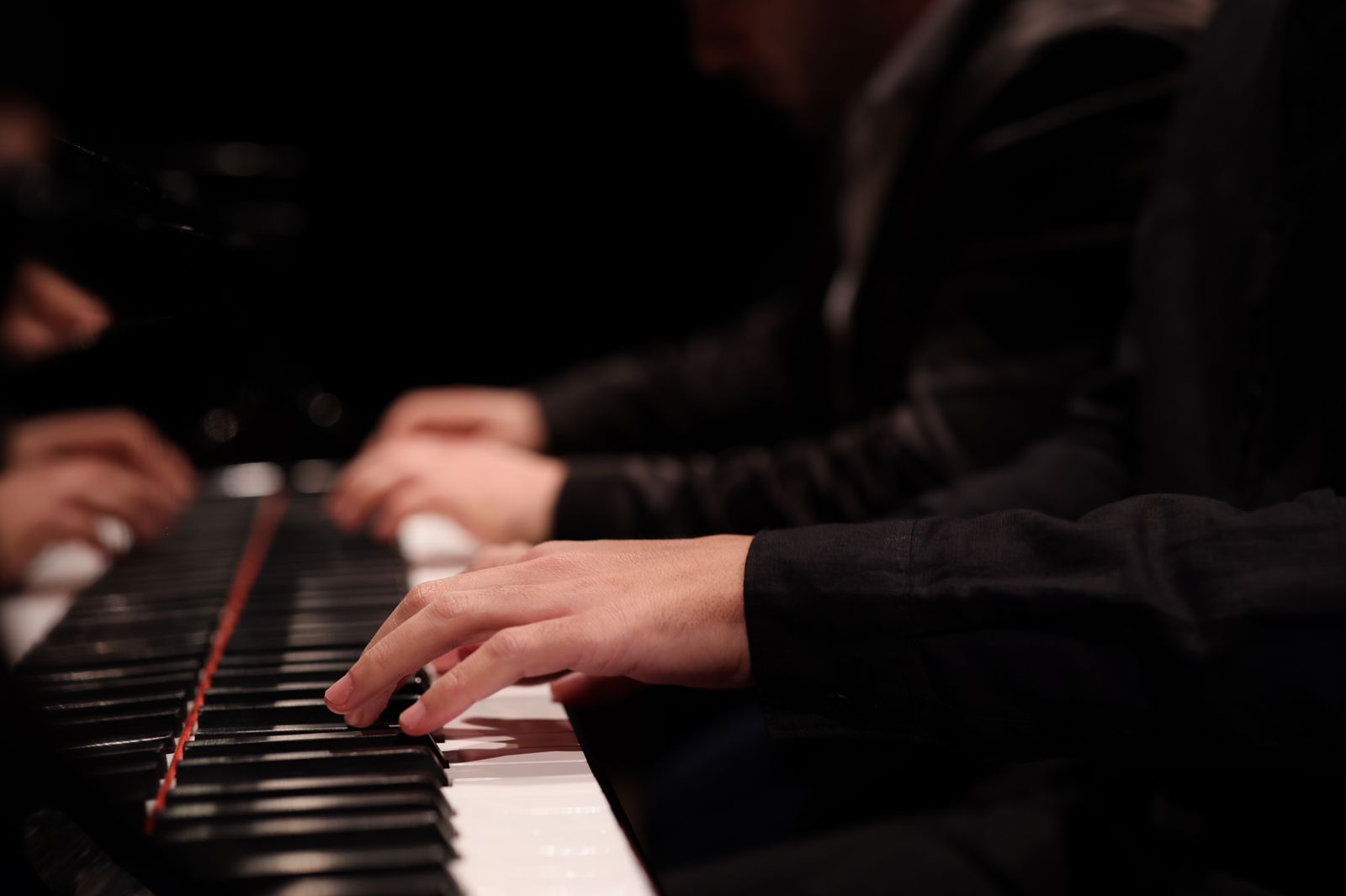 A imagem mostra quatro mãos tocando um piano.